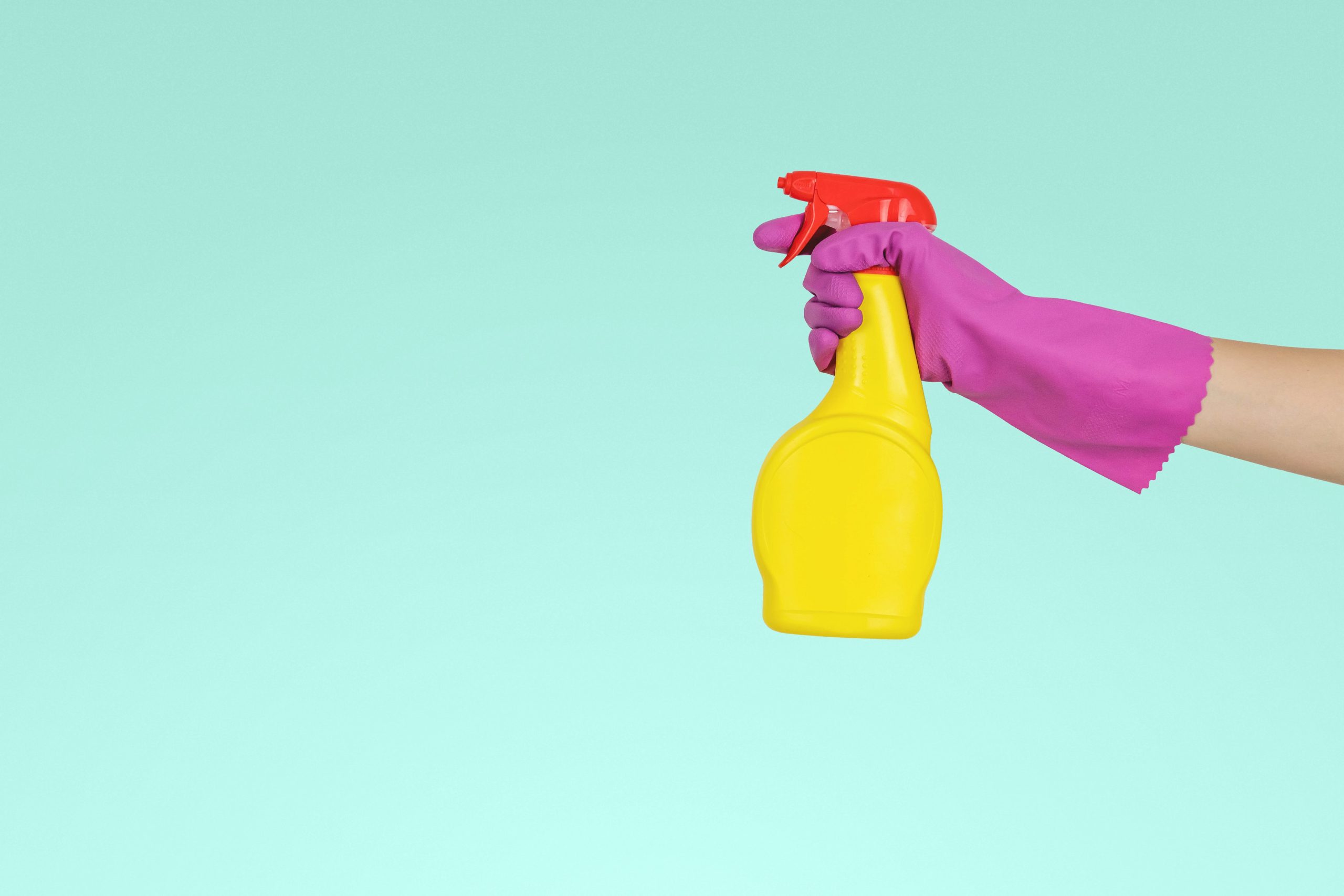 Person holding yellow bottle of cleaning spray and wearing cleaning gloves